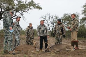 group of hunters in camo with two fresh deer kills